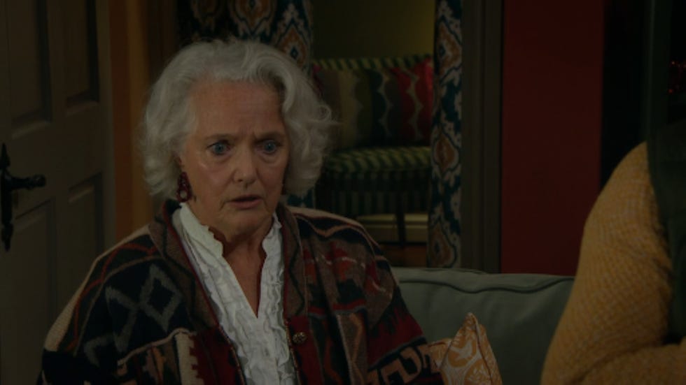 indoor scene with a seated person in a patterned cardigan and a visible couch