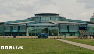 Exterior of the shopping centre- a green glass building with grass in the front.