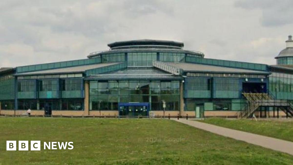 Exterior of the shopping centre- a green glass building with grass in the front.