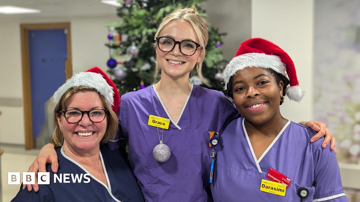 Three women in medical scrub. There is a Christmas tree behind them.
