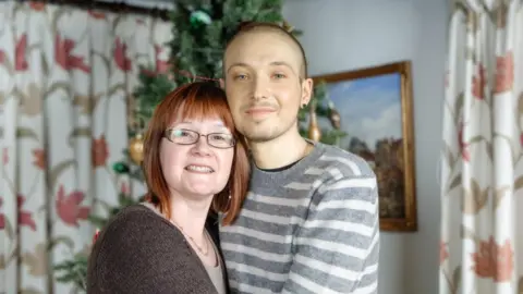 Supplied Robin Freeman has short hair and is wearing a grey and white striped top. He is hugging his mum, who has auburn hair and is wearing a brown cardigan. They are pictured in a room which features floral patterned curtains and pictures in the background.
