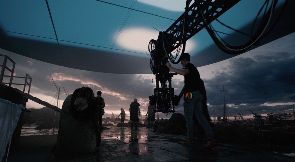 Film set with cranes and crew, under dramatic evening sky.