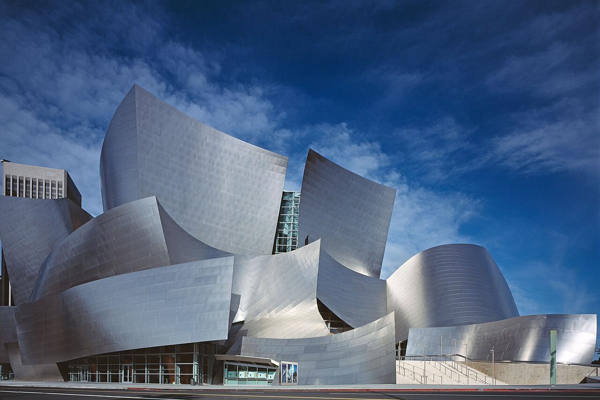 The Walt Disney Concert Hall, home to the Los Angeles Philharmonic, features an acoustically superior auditorium paneled in hardwood. Exterior view of Frank Gehry’s Walt Disney Concert Hall and its oddly curving and angled silvery shapes taken in Los Angeles on a clear, sunny day with a dark blue sky and wispy clouds in the background.