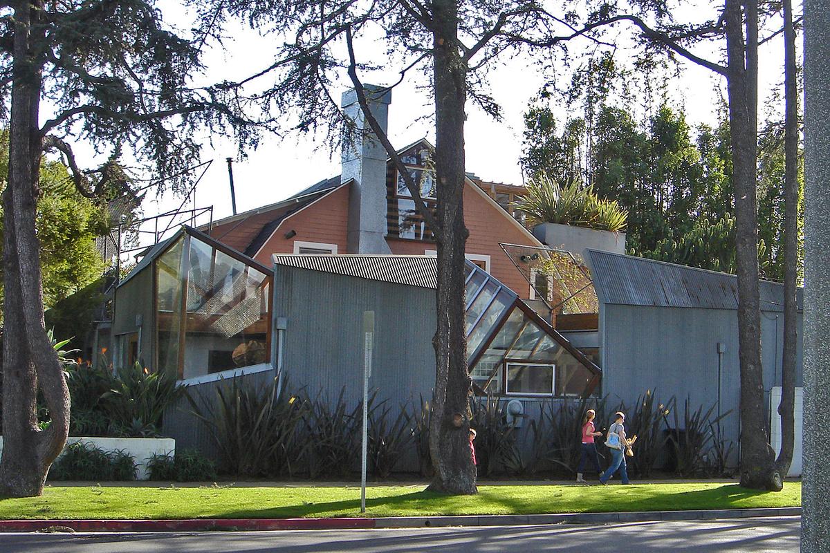 Frank Gehry's house in a posh area in Santa Monica. It is built upon an old house, with new elements added into the frame. The image shows two people walking past a structure with odd shapes and strangely protruding walls built around a more "normal" looking American house.