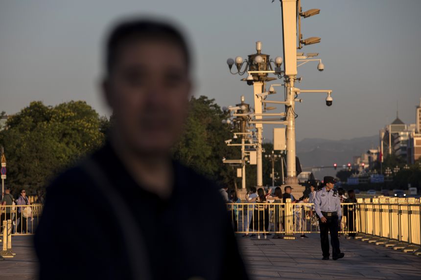 A police officer walks past surveillance cameras mounted on posts at Tiananmen Square in Beijing on May 31, 2019.