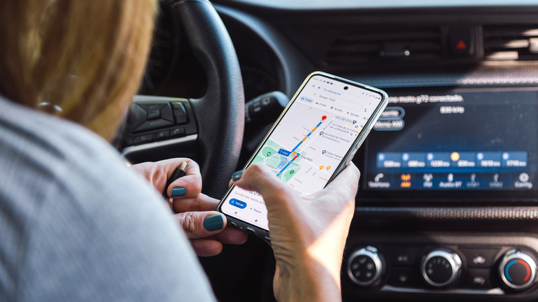 A woman using Google Maps on her phone in a car.