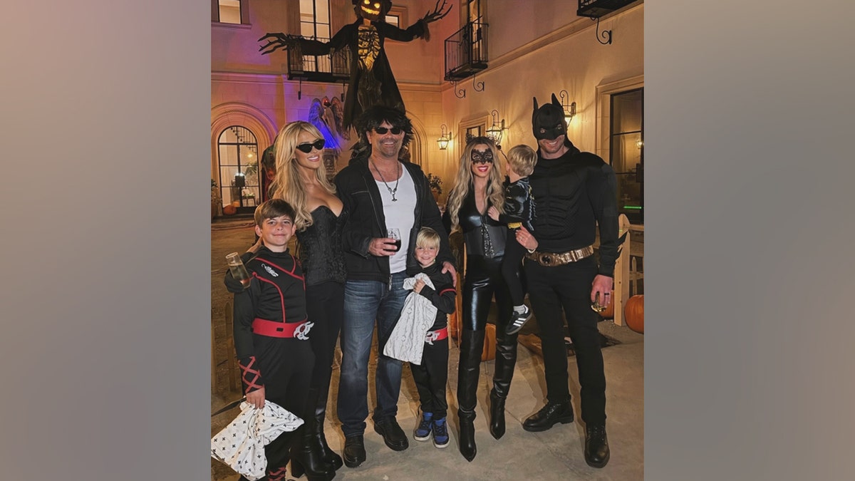 Christina Haack posing with Heather Rae and Tarek El Moussa and their children in Halloween costumes in front of spooky decorations.
