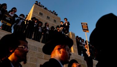 Ultra-Orthodox Jewish men stand on a building and hold protest signs during a large anti-draft rally in Jerusalem.