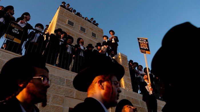Ultra-Orthodox Jewish men stand on a building and hold protest signs during a large anti-draft rally in Jerusalem.