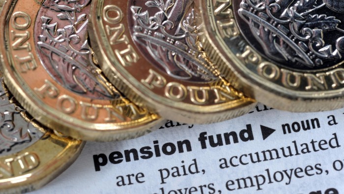 Several British one-pound coins resting on a dictionary page showing the definition of ‘pension fund’.