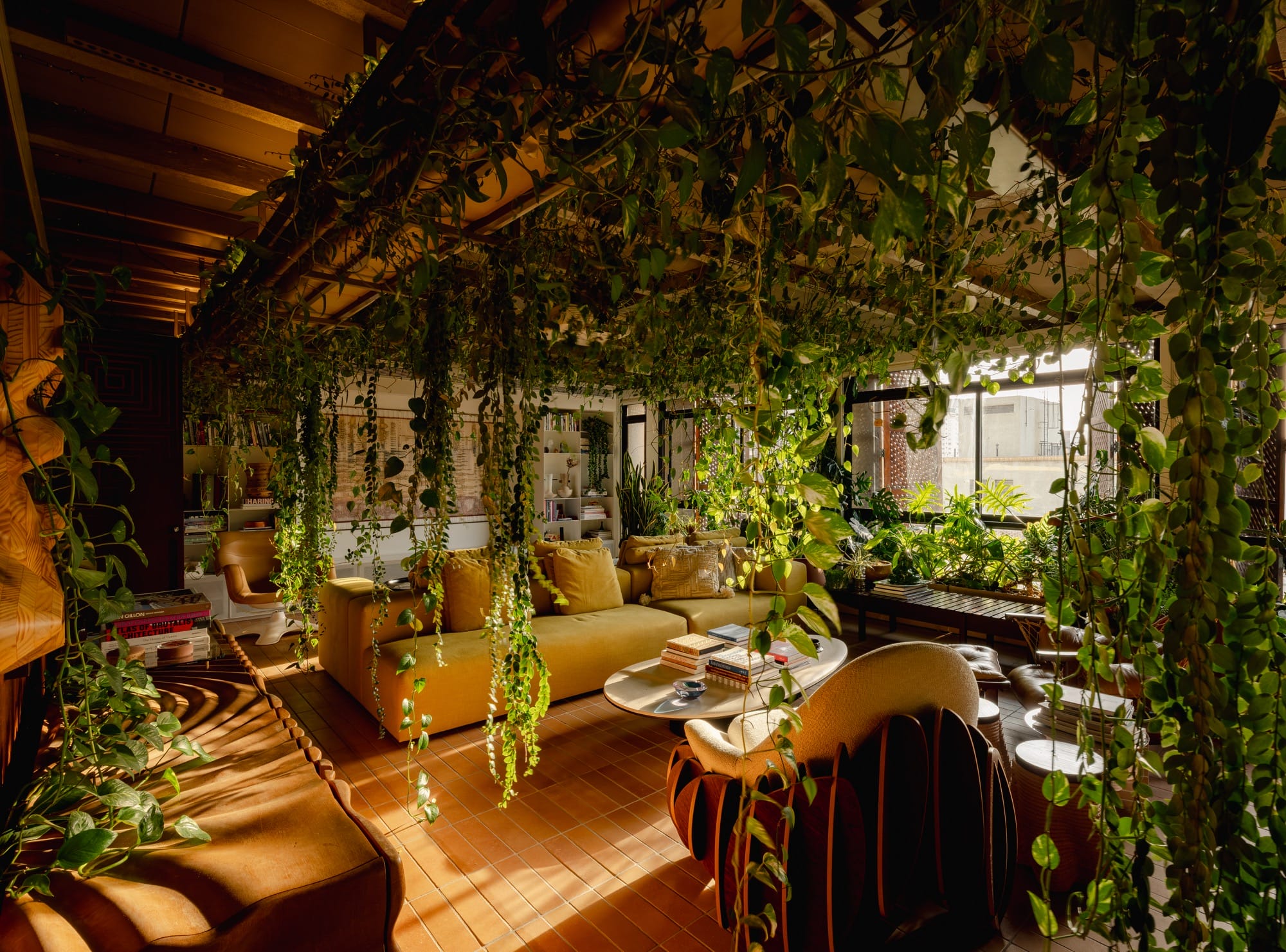 An apartment interior designed by Guto Requena with an eclectic variety of contemporary furnishings and houseplants draping from rafters in the ceiling