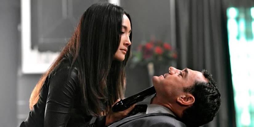 Nikita holds a gun to a man's chin in a room.