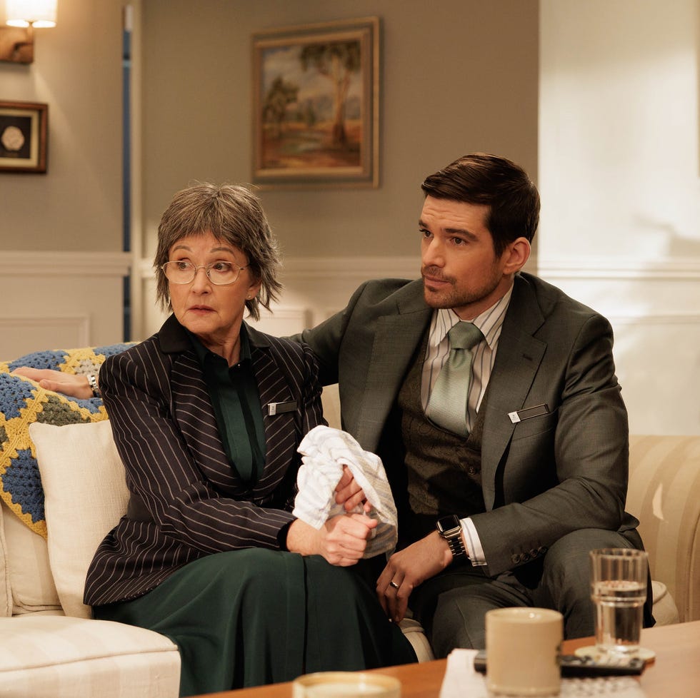 two people seated on a couch in a living room one holding an item a relaxed but serious atmosphere two people seated on a couch in a living room one holding an item a relaxed but serious atmosphere