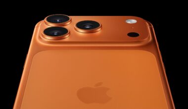 Close-up of the back of an orange iPhone, showing three camera lenses, a flash, and the Apple logo against a black background.
