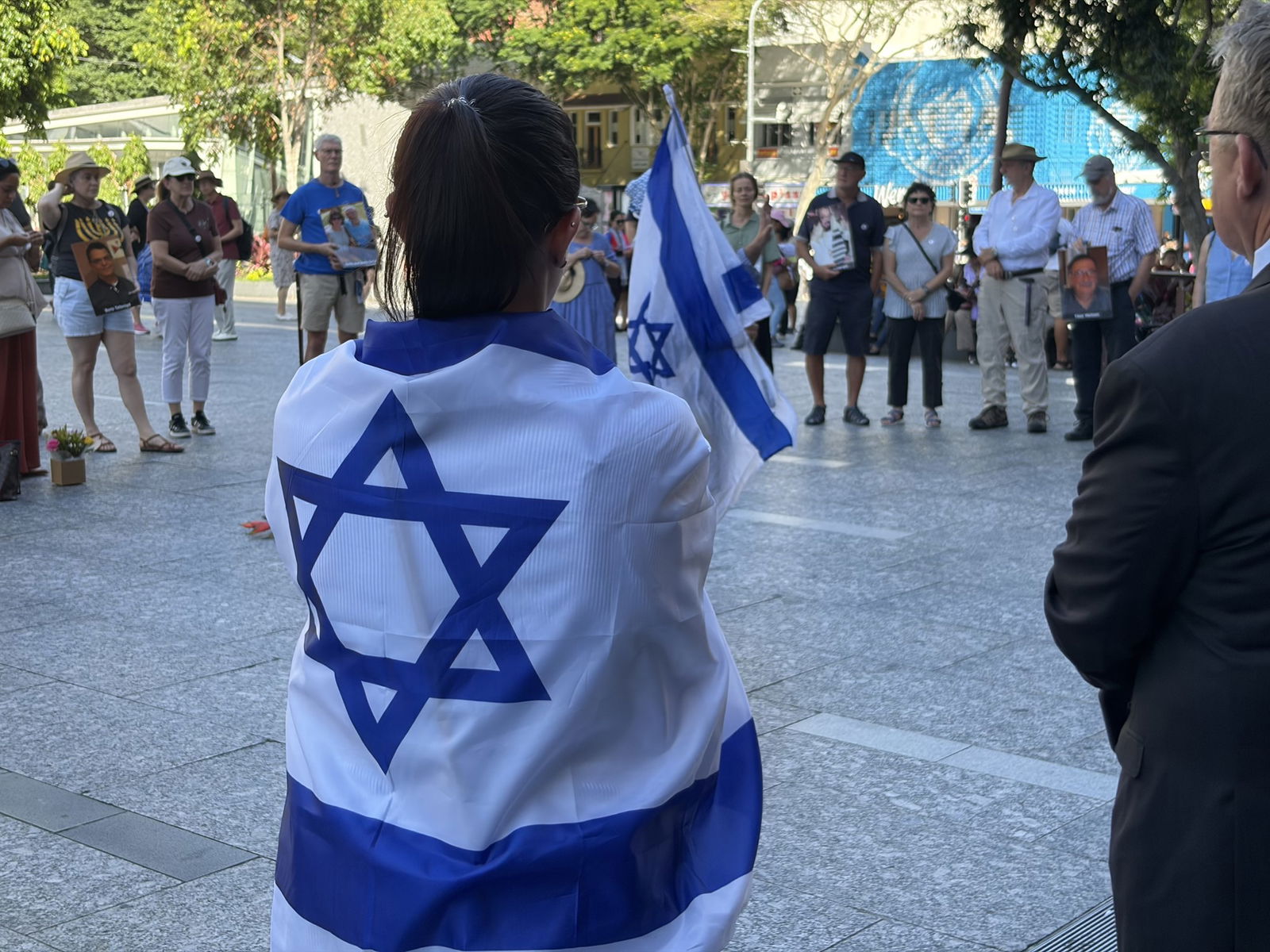 A woman with long dark hair with an Israeli flag draped around her stands in front of a crowd.