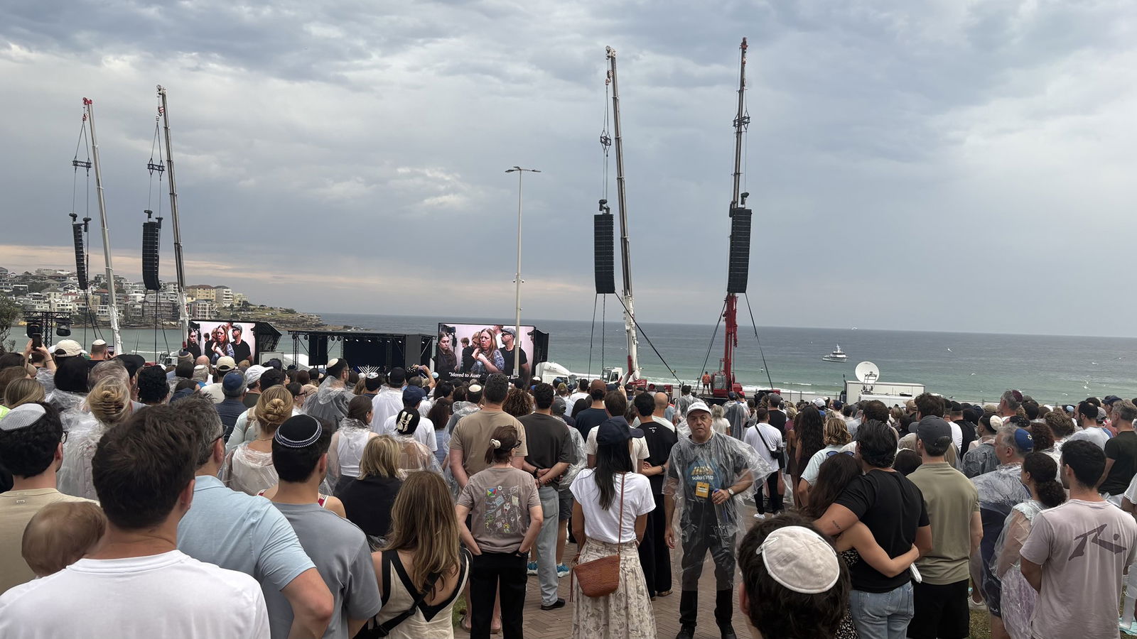 a crowd on a beach with a small white boat in distance