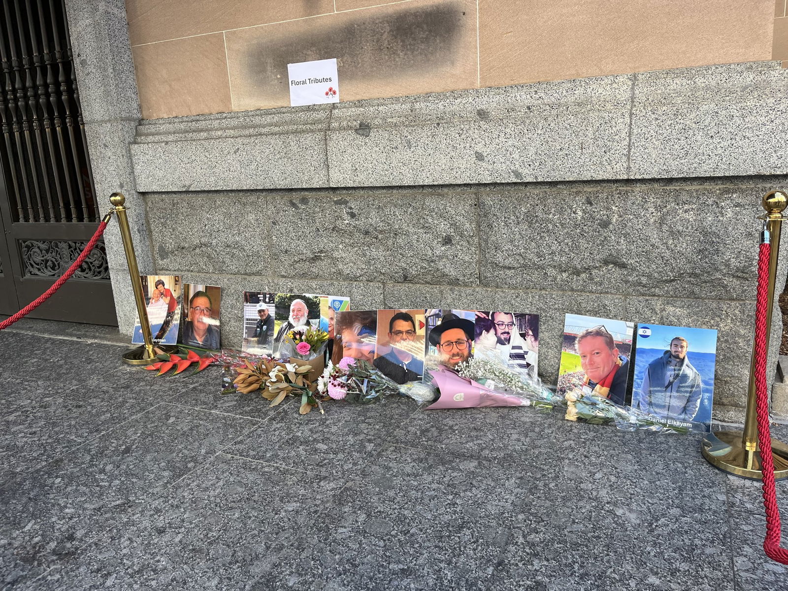 Flowers lie beside photos of people that are propped against a building.