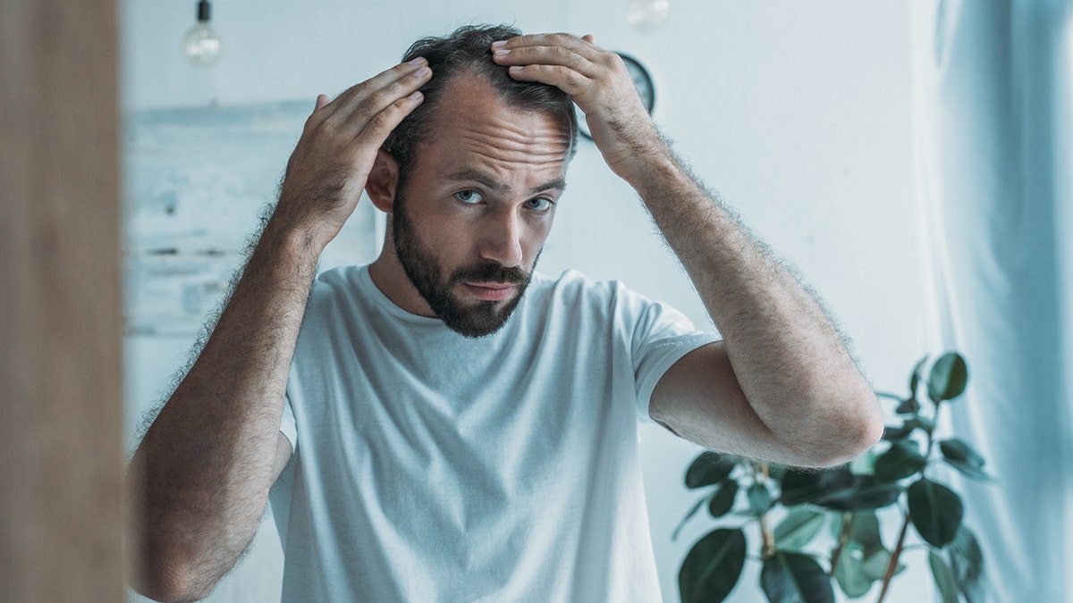Man inspecting hair loss in mirror