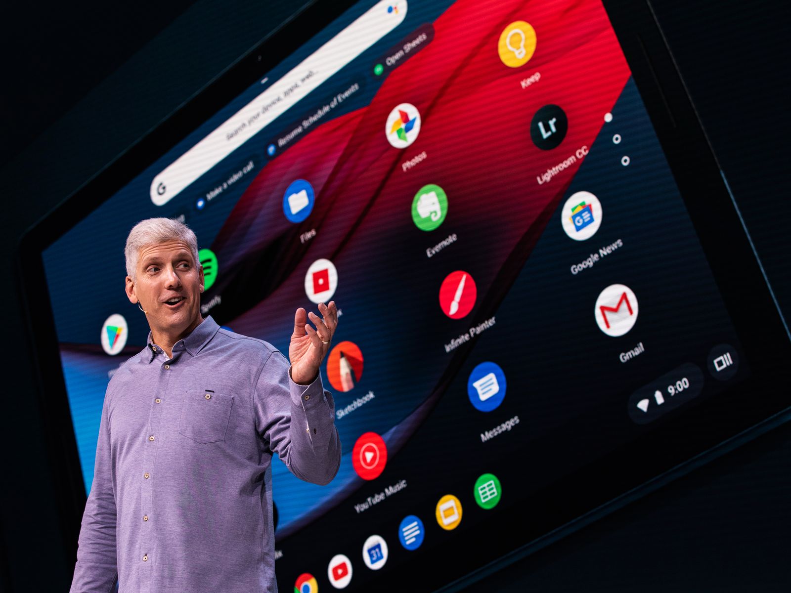 Person in purple longsleeve shirt gesturing toward a large screen behind them