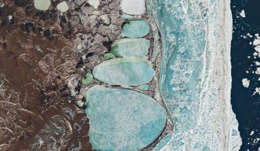 A Landsat image of Russia’s Chukchi Peninsula shows a narrow coastal sandspit separating the Arctic Ocean from a chain of elongated, ice-covered coastal lagoons near the village of Billings and Cape Billings. The pale blue lagoons vary in size and line up end-to-end, creating a shape that resembles a snowman pressed against the shoreline. Offshore, fractured sea ice forms a bright, textured band along the coast, while darker tundra and thermokarst lakes extend inland.