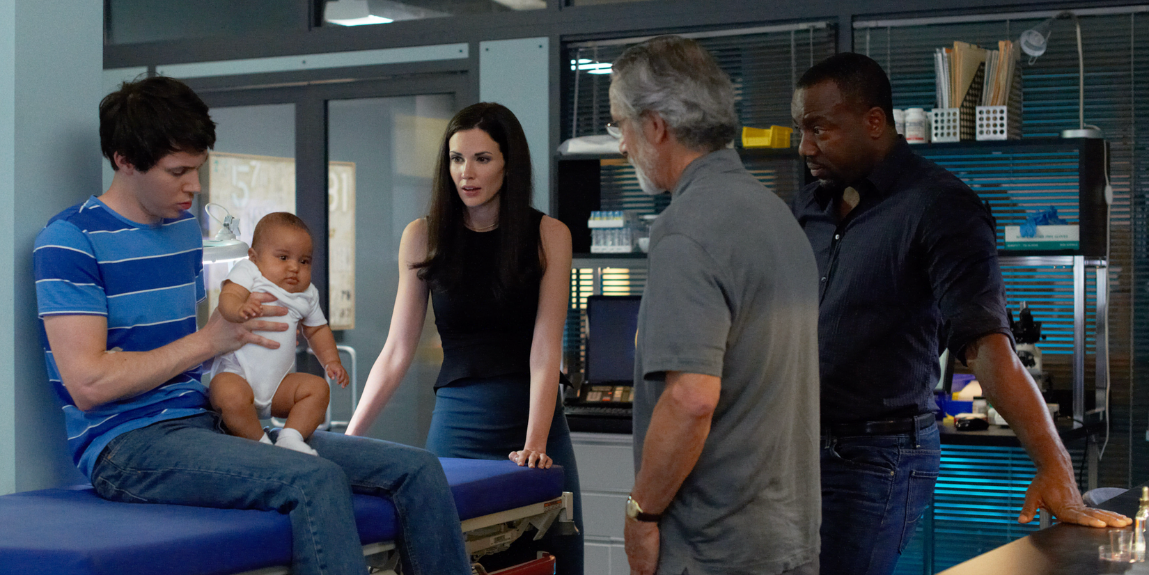 Ryan Carwright (holding baby), Laura Mennell, David Strathairn (back to camera), Malik Yoba stand in their medical office.