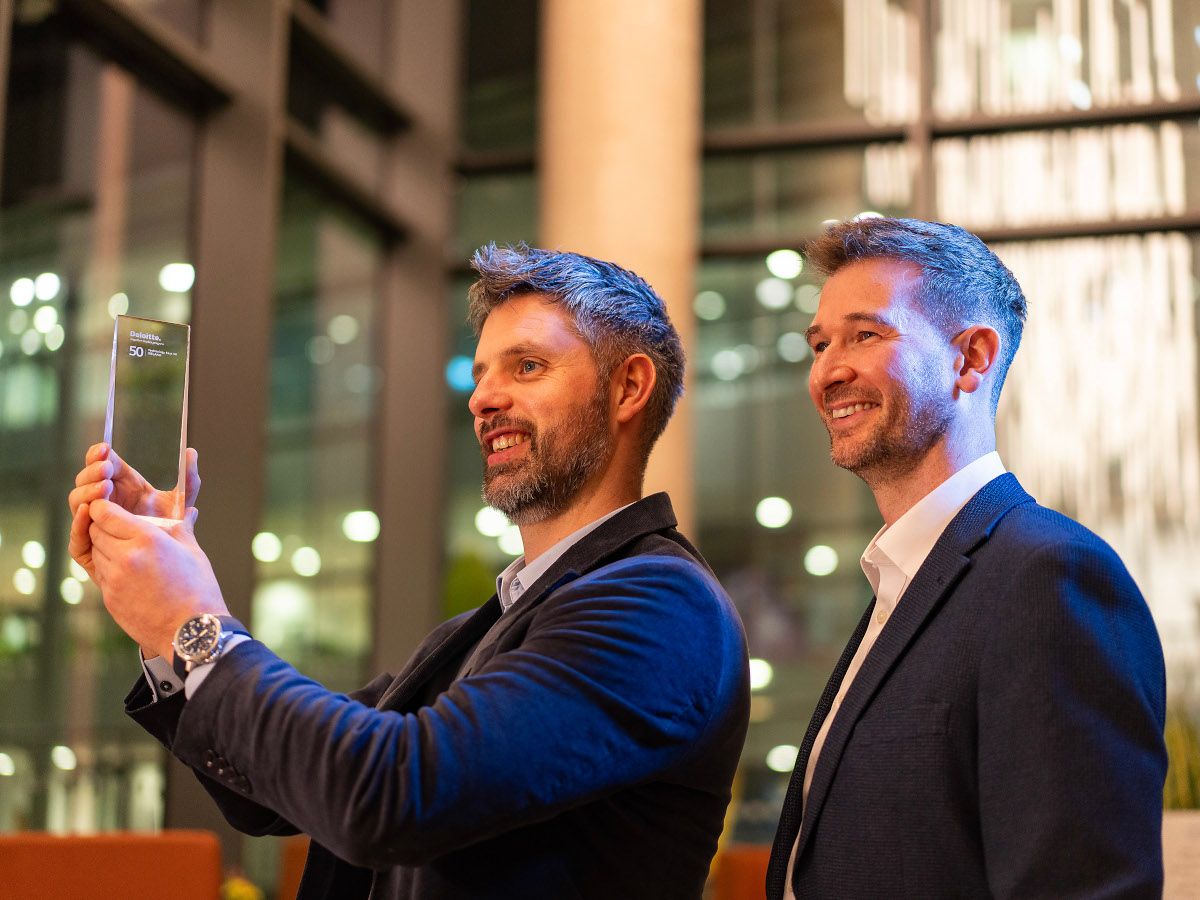 Two men, one holding a glass award trophy, stand next to each other smiling and looking to the left side of the photo.