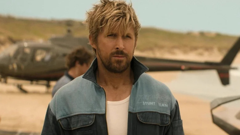 Colt Seavers (Ryan Gosling) stands in a stunt jacket with a helicopter in the background in The Fall Guy