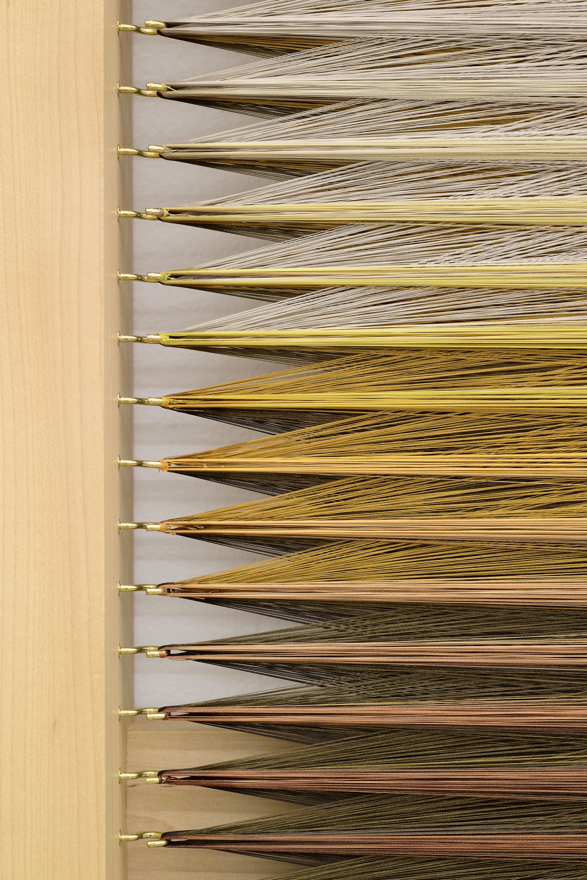 A detail of an abstract weaving by Rachel Mica Weiss of a purple-yellow-brown gradient made with numerous strands of embroidery thread pulled with tension within a maple frame