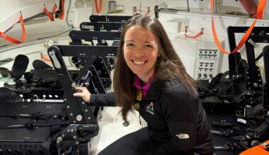 A woman crouches inside the mockup of a spacecraft that is equipped with seats for crewmembers.