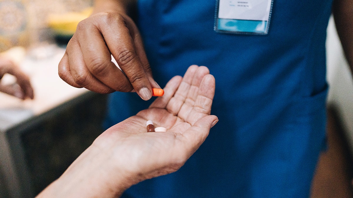 Nurse's hand giving medicine to a senior woman patient