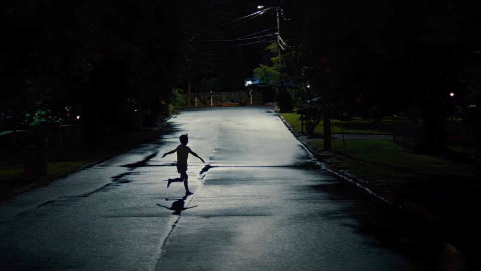 A shadowy image of a child running with his arms out into the street in the dead of night in a scene from Weapons. 