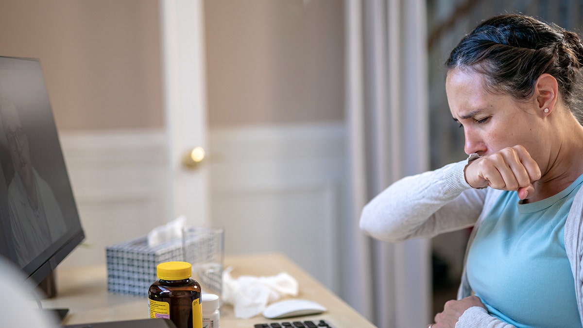 Woman coughing at desk at home.