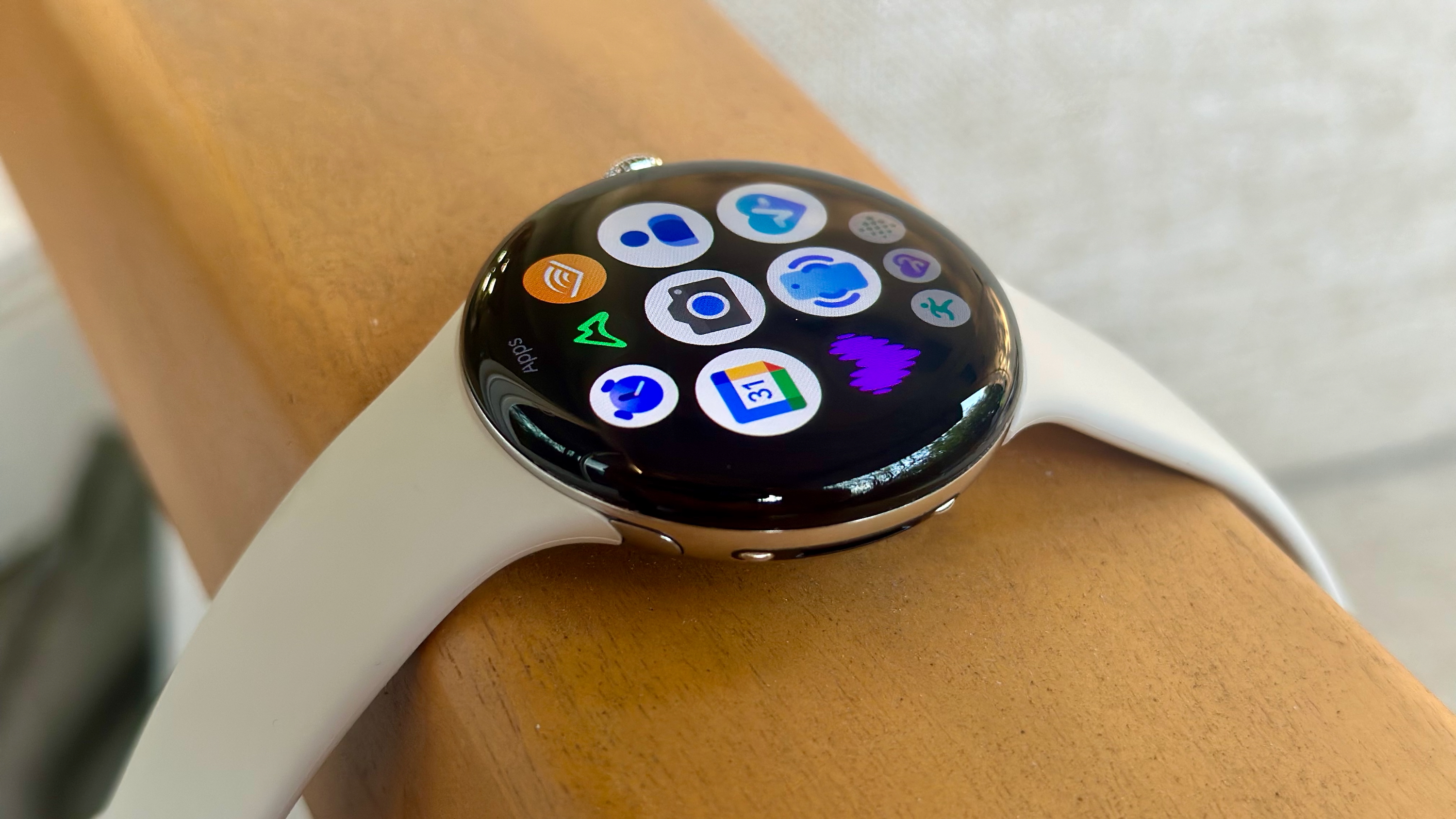 The Google Pixel Watch 4 sitting on an armrest with the app drawer icons visible on the Actua 360 display.