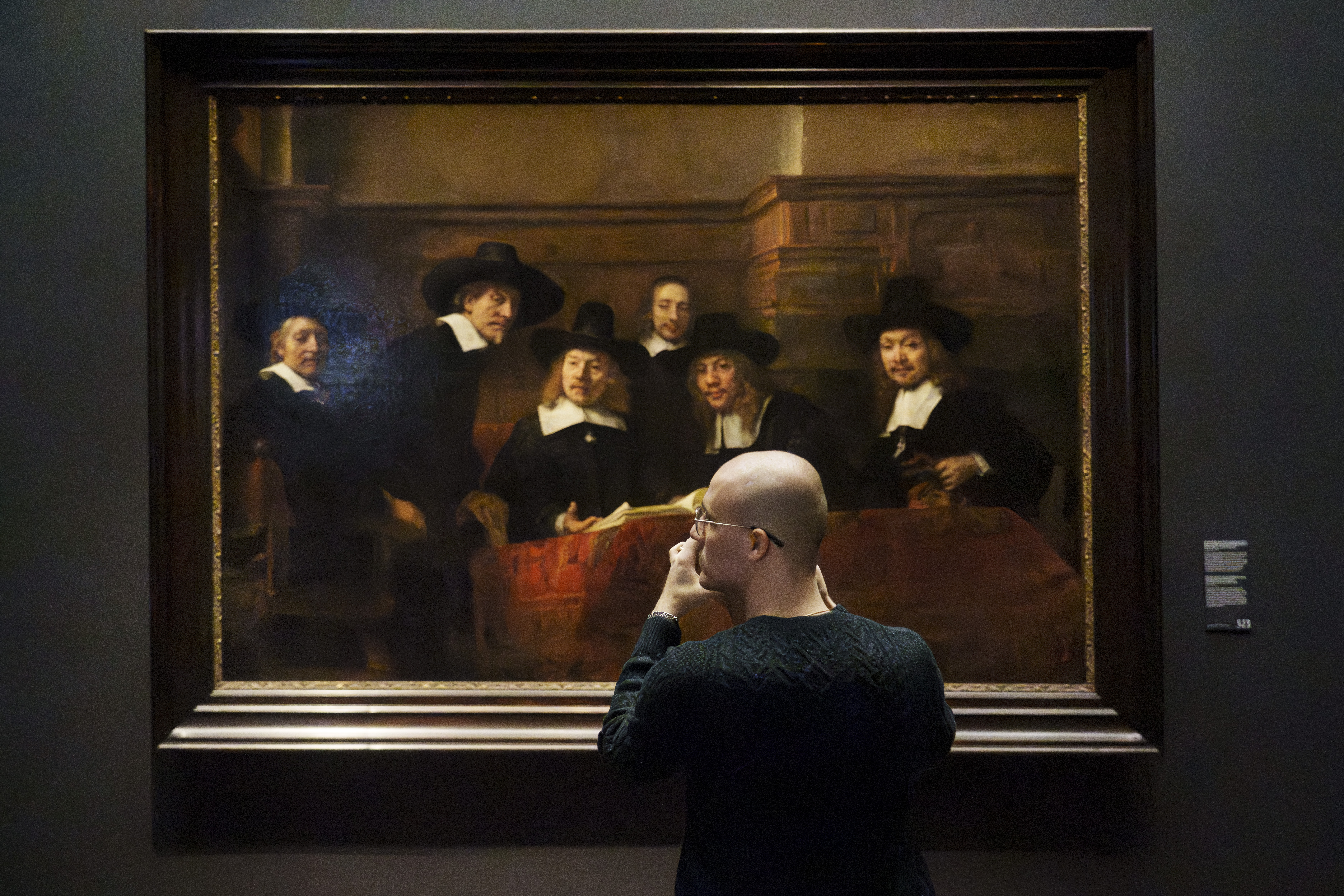 A visitor looking at Rembrandt's painting, "The Syndics of the Drapers' Guild," in the Rijksmuseum, Amsterdam.