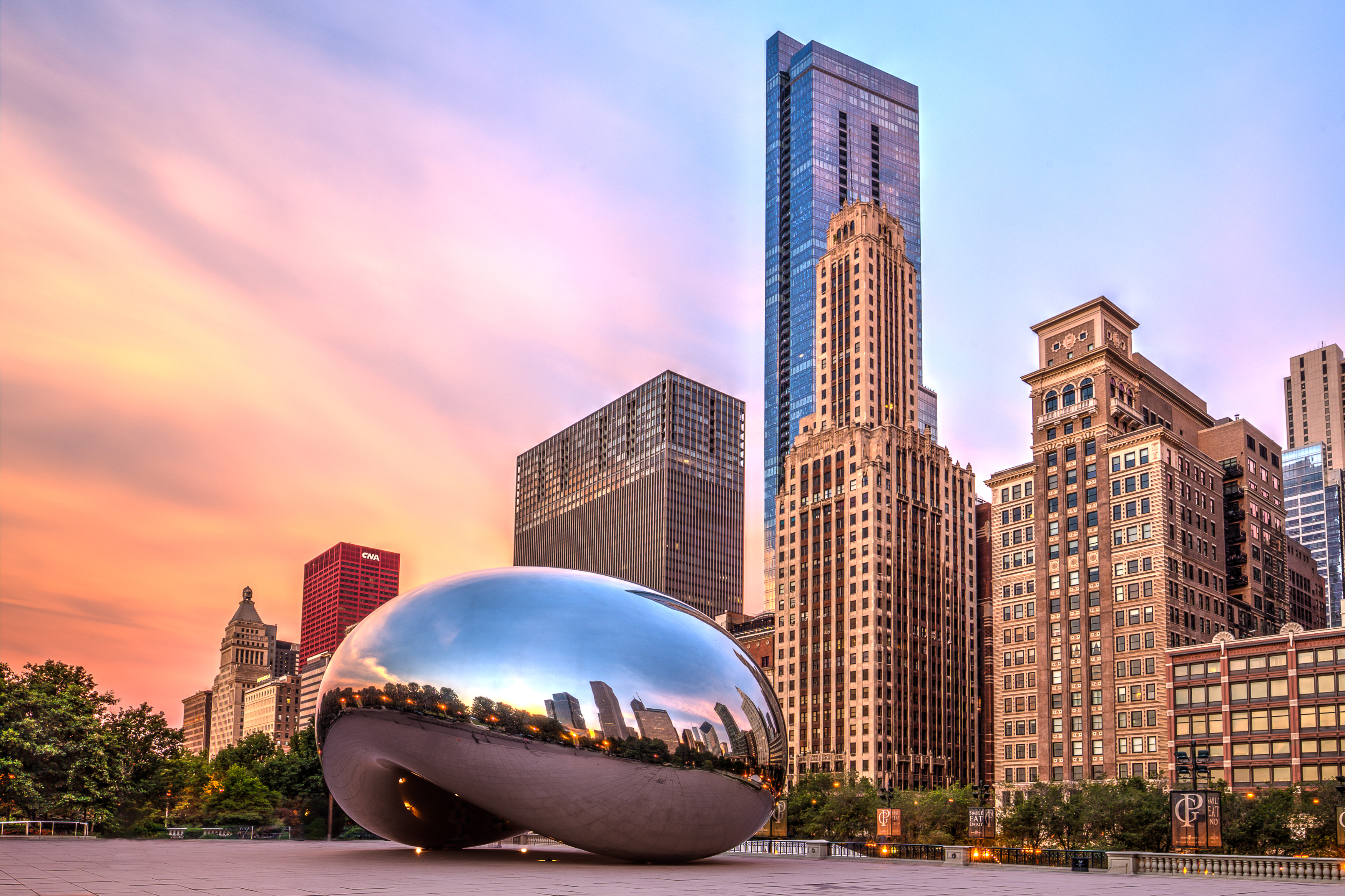 The Cloud Gate sculpture in Millennium Park, Chicago, reflecting city buildings and a colorful sunrise sky.