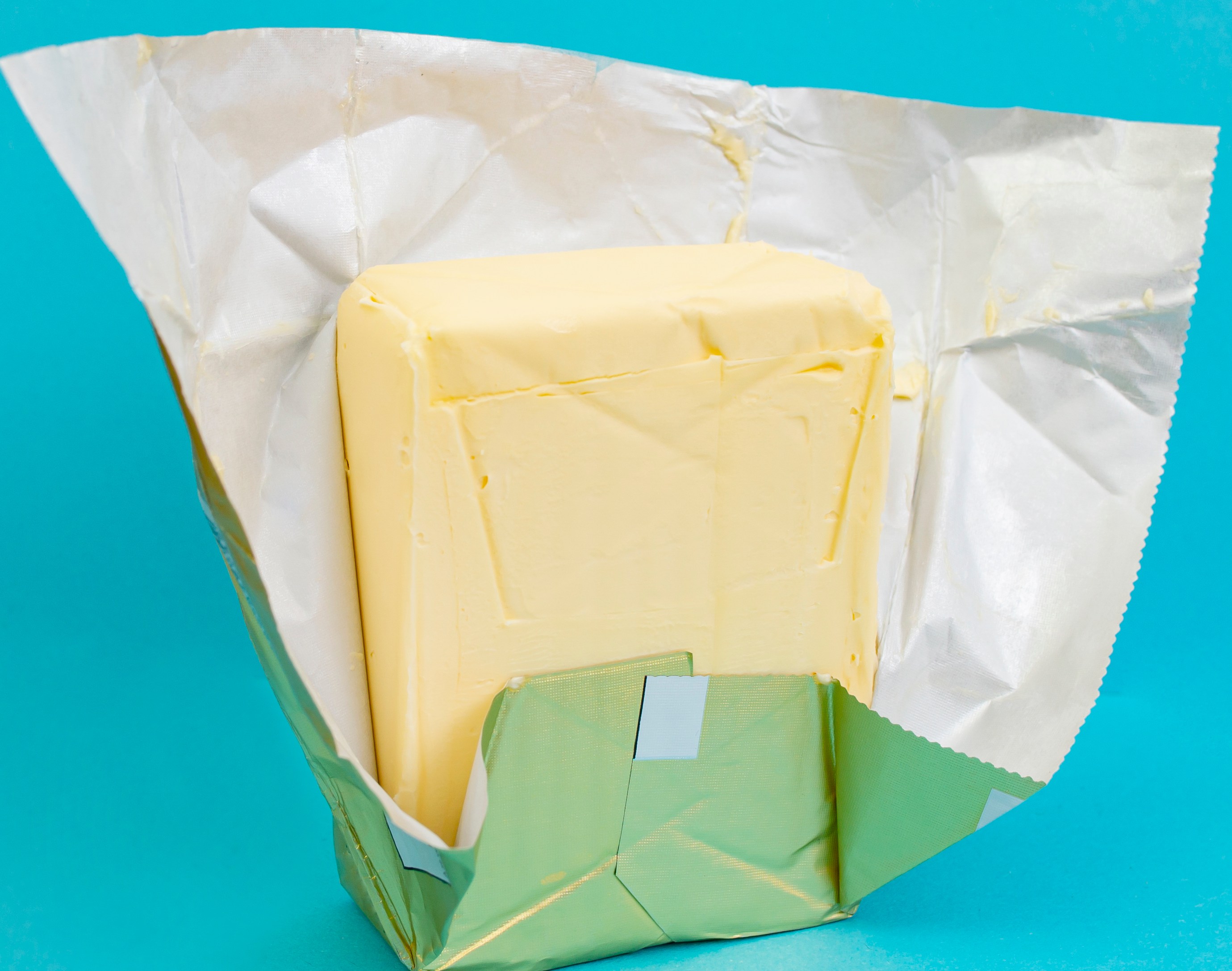 Yellow butter stick in a golden foil pack on a blue background.