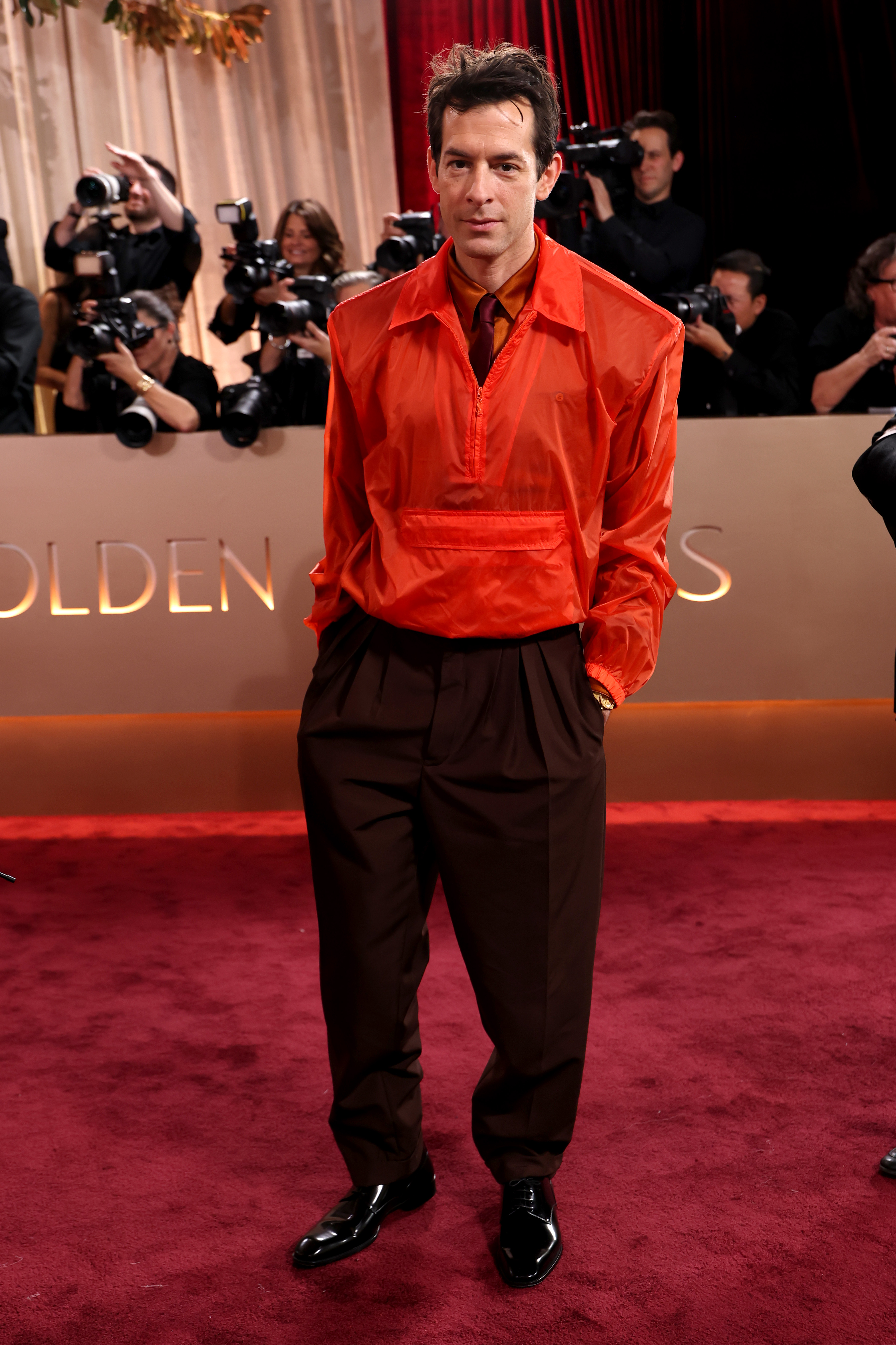 Mark Ronson attends the 83rd annual Golden Globe Awards wearing an orange jacket, brown pants, and black shoes.