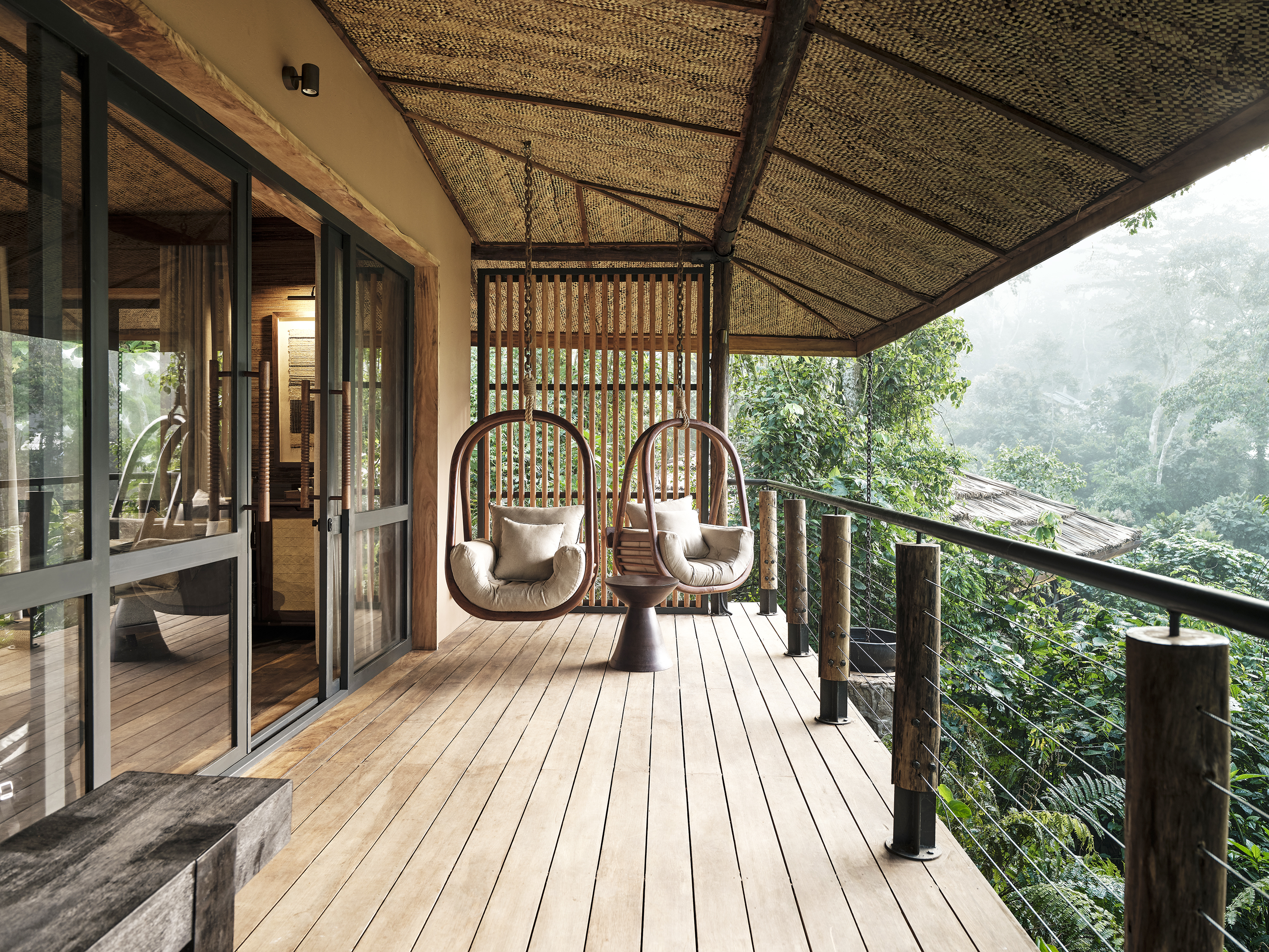 A luxurious balcony with two hanging chairs overlooking a misty Ugandan forest.