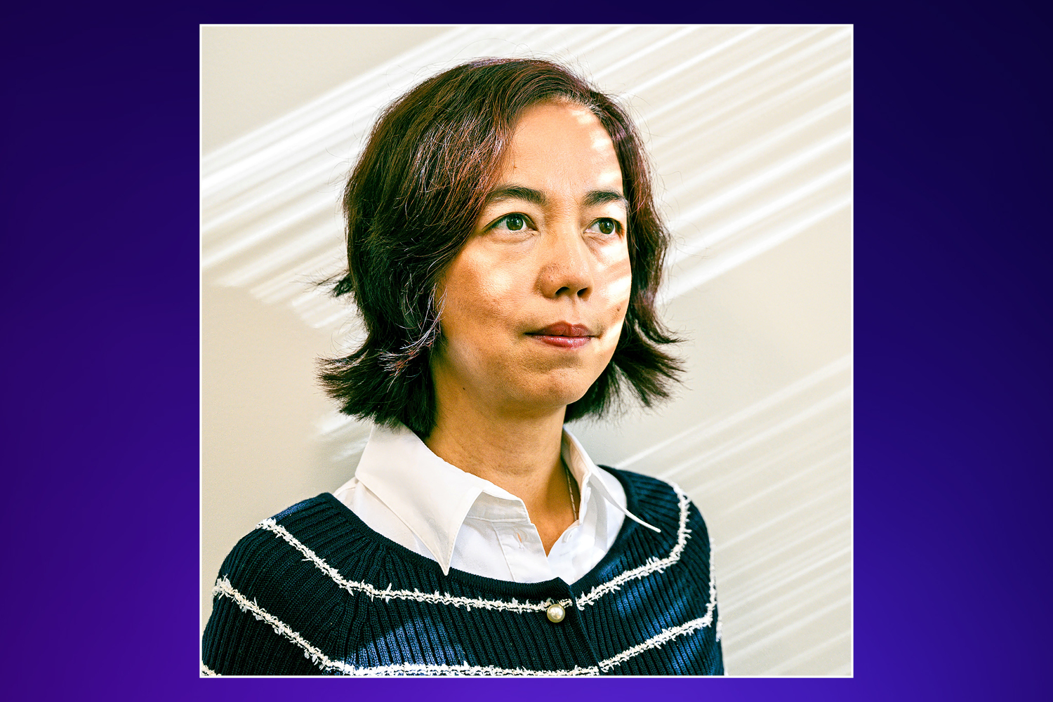 A woman with short dark hair in a white collared shirt and dark blue cardigan with white stripes.