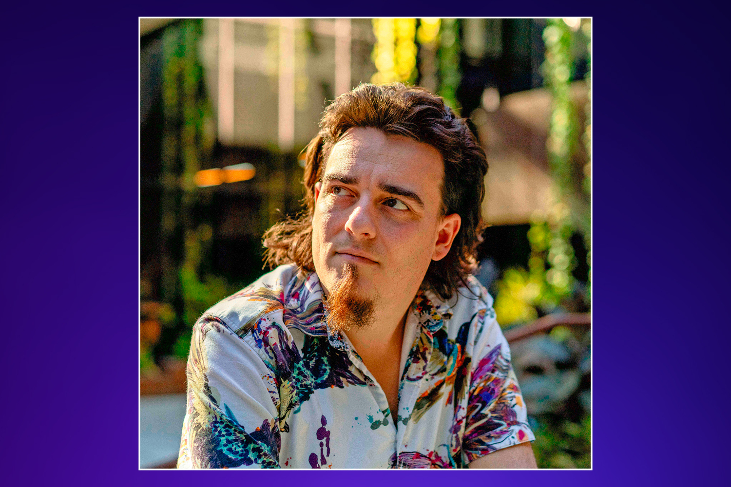 A man with a goatee and colorful shirt looking to his left.