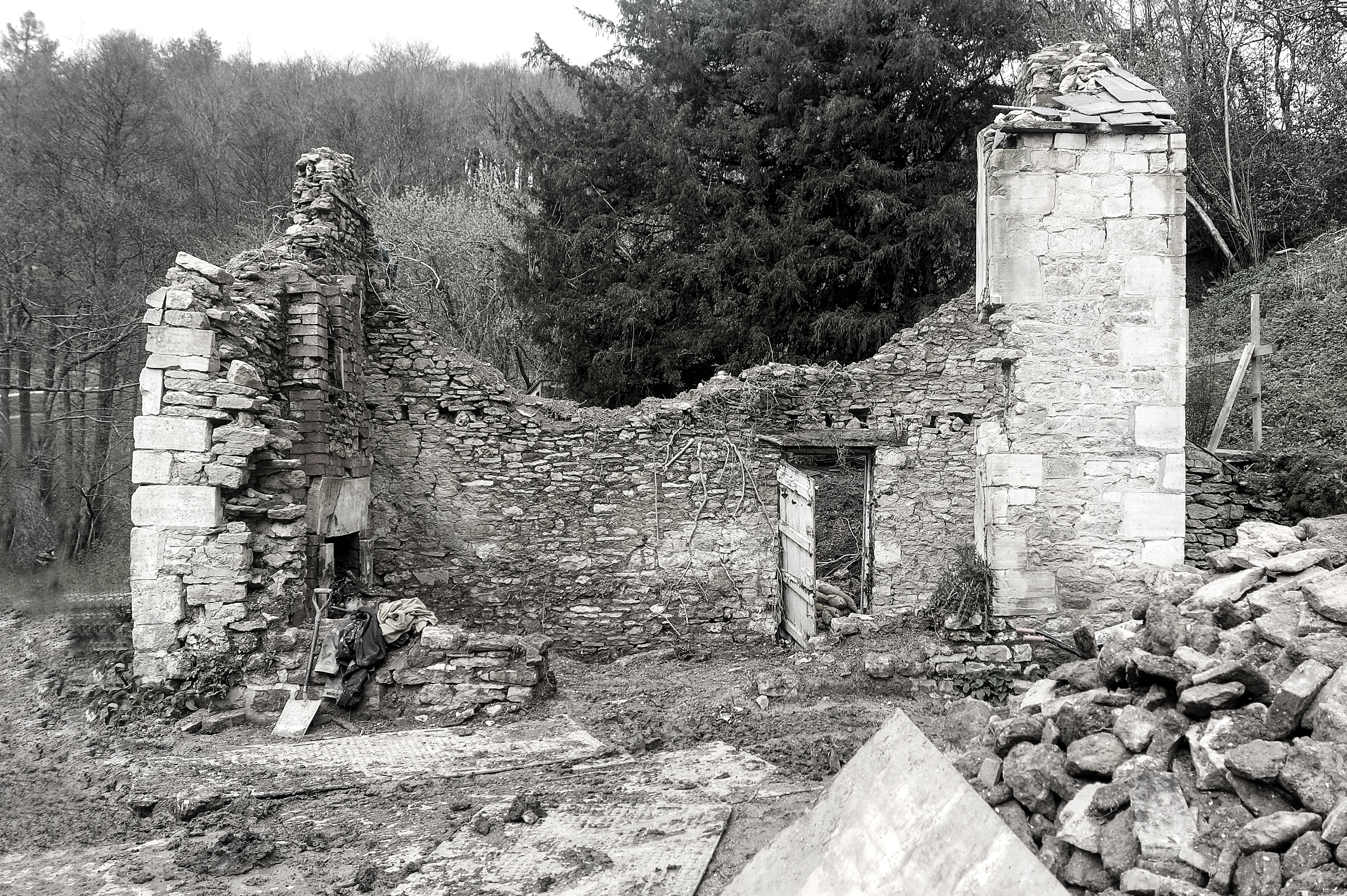 Timbercombe Cottage ruins, featuring stone walls and an open wooden door, surrounded by trees.