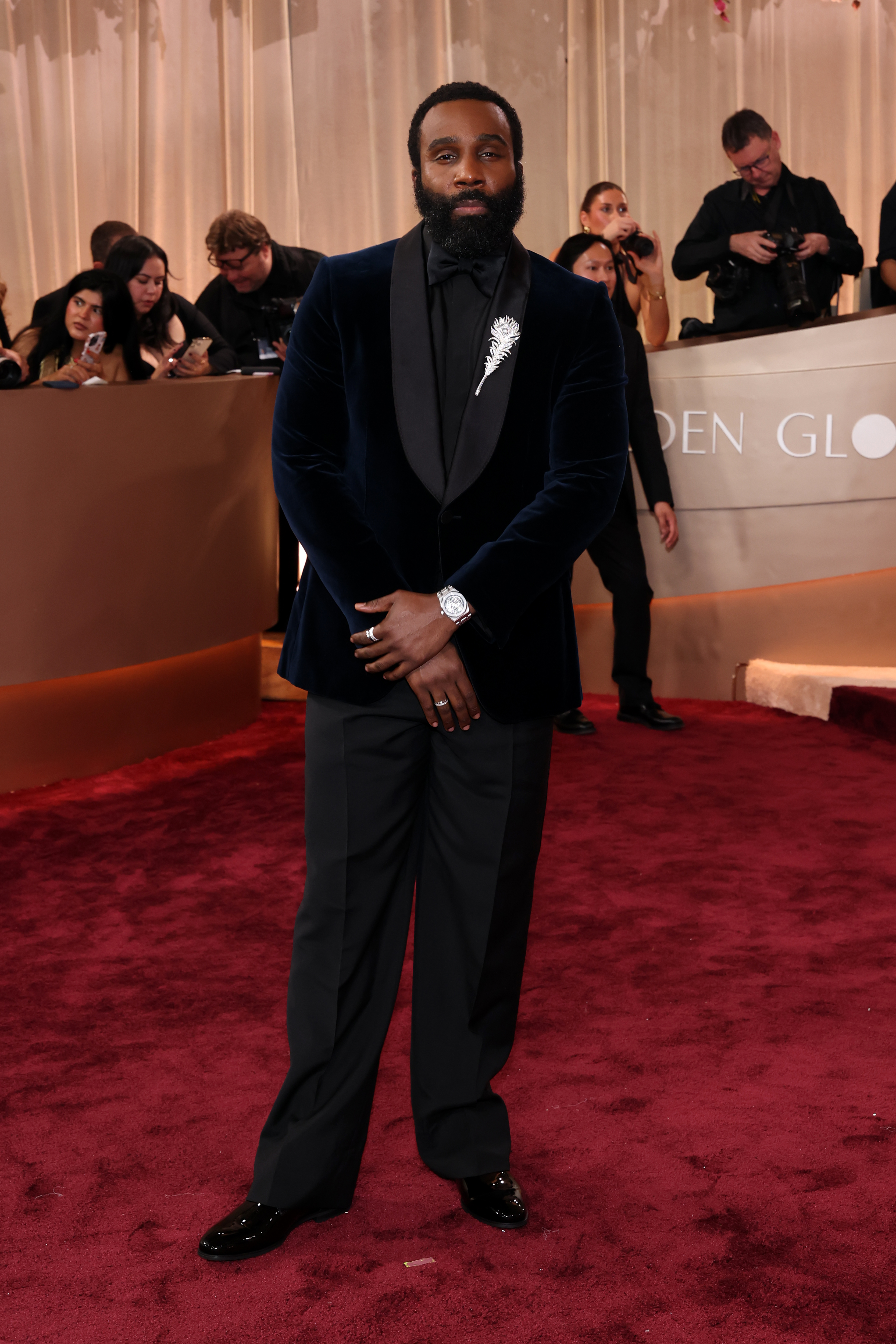Tramell Tillman poses on a red carpet in a dark blue velvet jacket with a feather brooch.