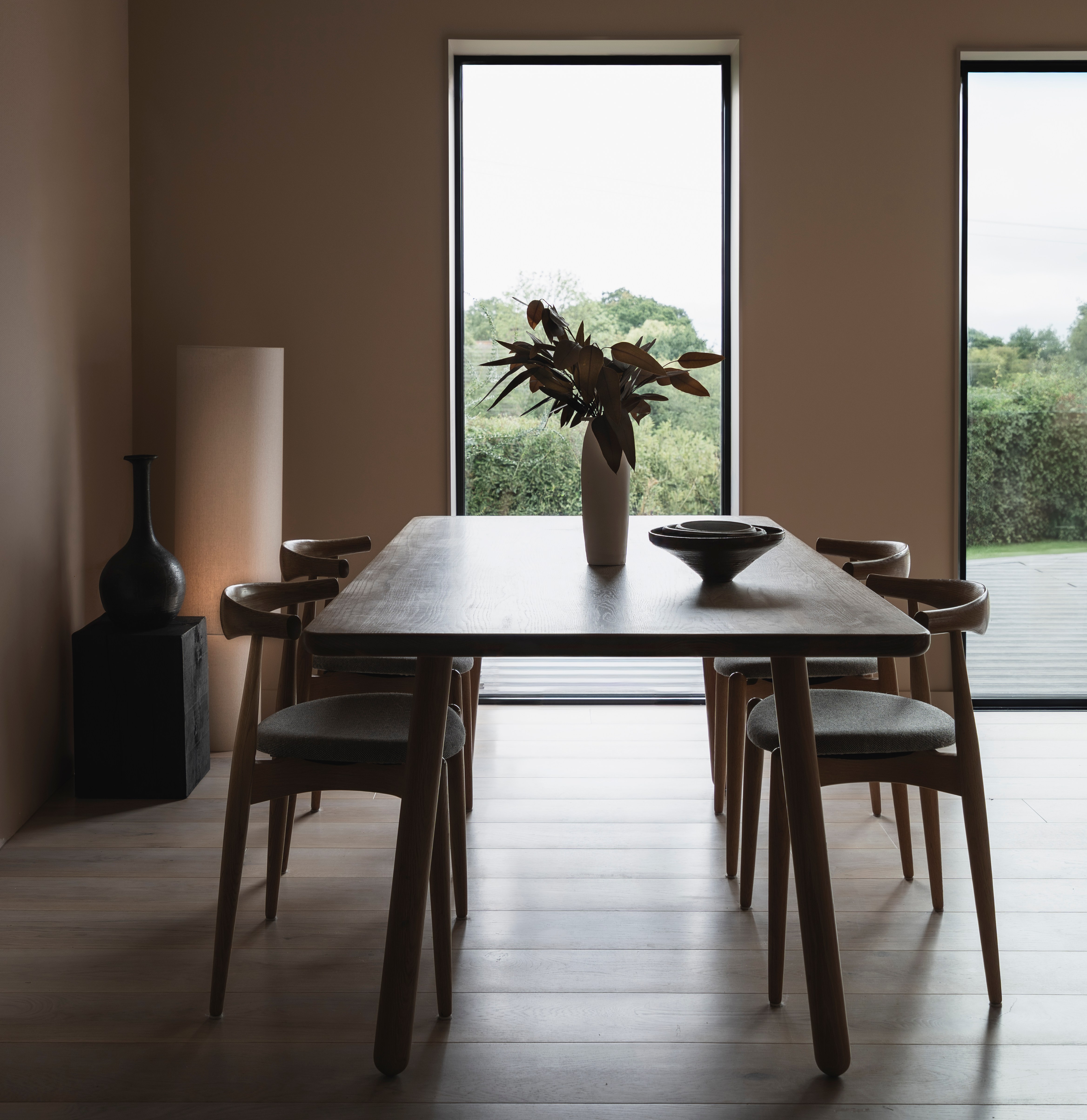 Dining room with large windows showing lush greenery outside.