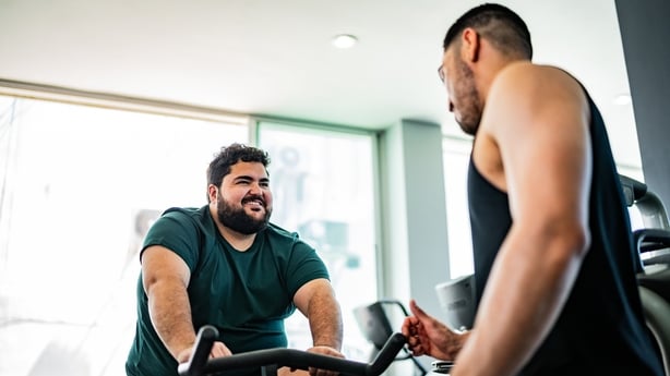 man talking to instructor on exercise bike at gym