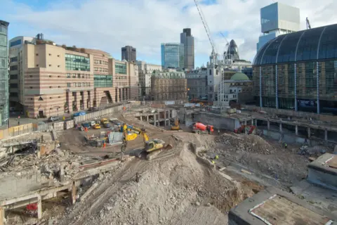 Mola Wide shot showing various construction vehicles digging in the dirt in central London with towers from the London skyline in the background