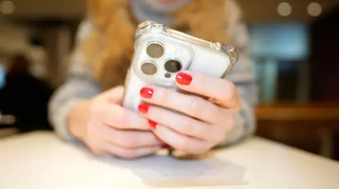 AFP via Getty Images A woman with nails painted bright red holds her mobile phone