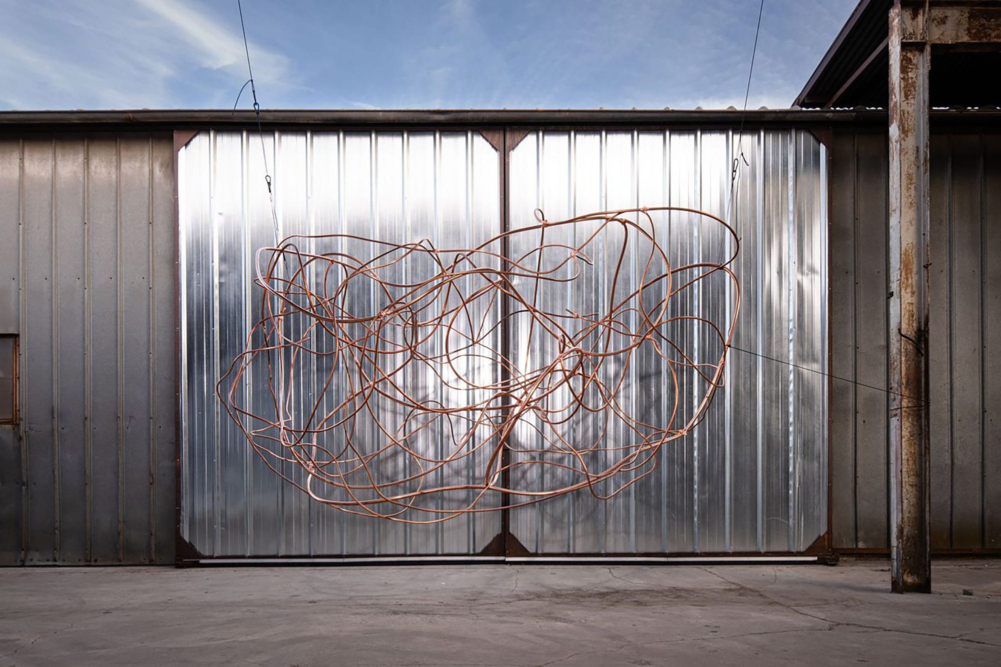 Copper wire sculpture against a metallic wall.