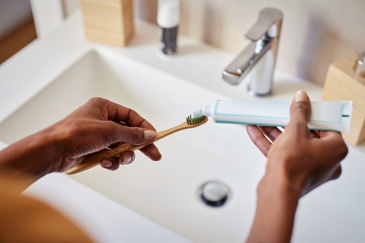 Black woman hand squeezing whitening paste on wooden toothbrush, taking care about mouth hygiene. Close up of female hands applying toothpaste on ecological bamboo tooth brush, plastic free concept. Oral hygiene and environmental responsibility concept.