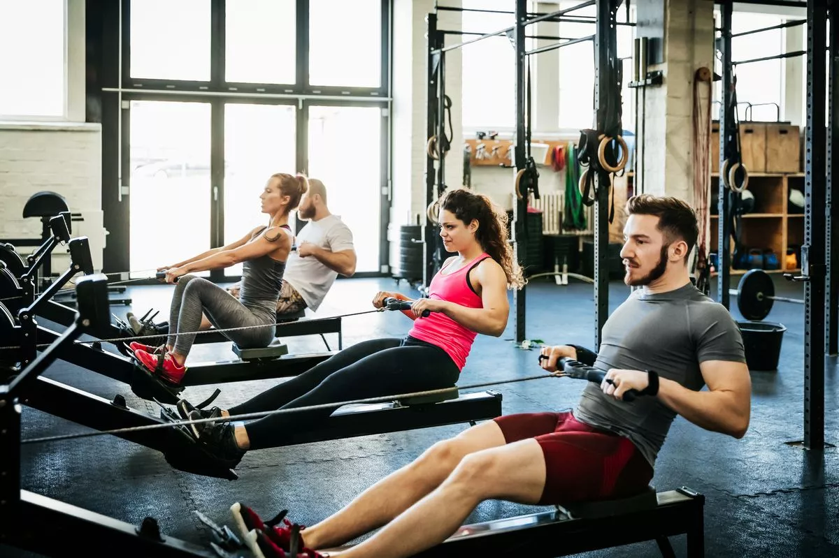 A group of fitness enthusiasts working out together at the gym using rowing machines - stock photo