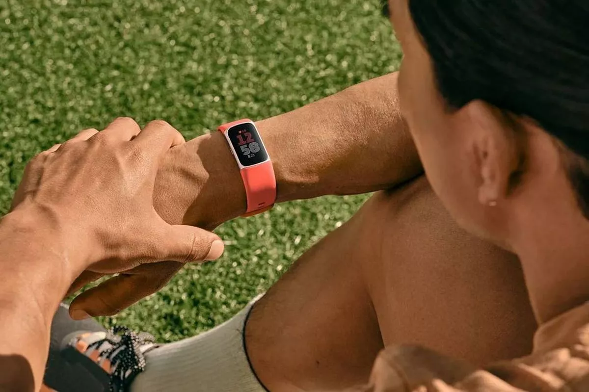 An individual is lying on a grassy surface, closely examining a digital wristwatch with a red strap. The person is dressed in athletic attire, suggesting they might be engaging in physical activities.
